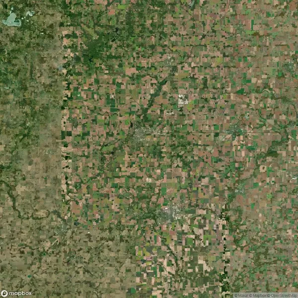 Aerial view of a vast, patchwork landscape consisting of fields and farmland with various shades of green and brown, intersected by roads.