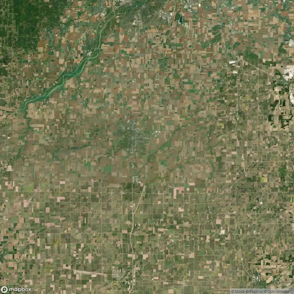 Aerial view of agricultural fields in a checkered pattern, with a river running through the green landscape. Sparse urban areas are visible in the distance.