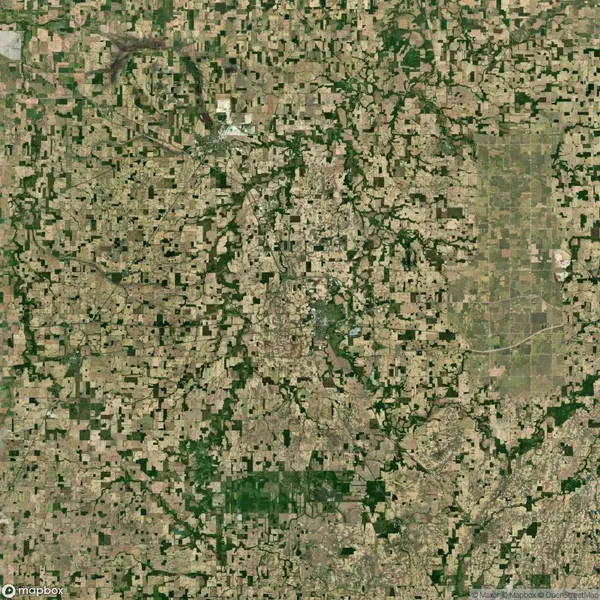 Aerial view of a landscape with a patchwork of agricultural fields and green areas scattered across, featuring a central cluster suggesting a town or city.