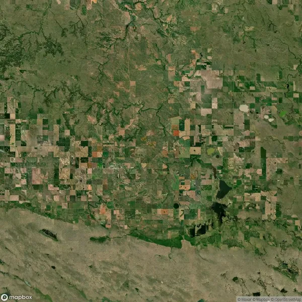 Aerial view of a patchwork landscape with various shades of green and brown fields, intersected by roads and small water bodies.