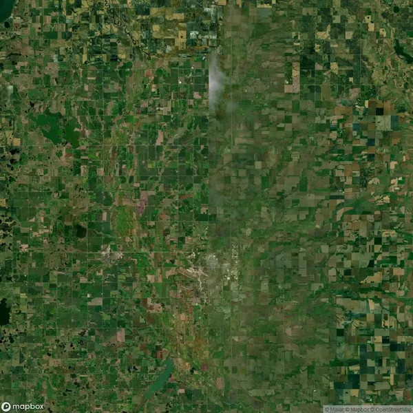 Aerial view of a rural landscape with visible agricultural fields in a grid pattern and a faint vertical line suggesting smoke or cloud cover.