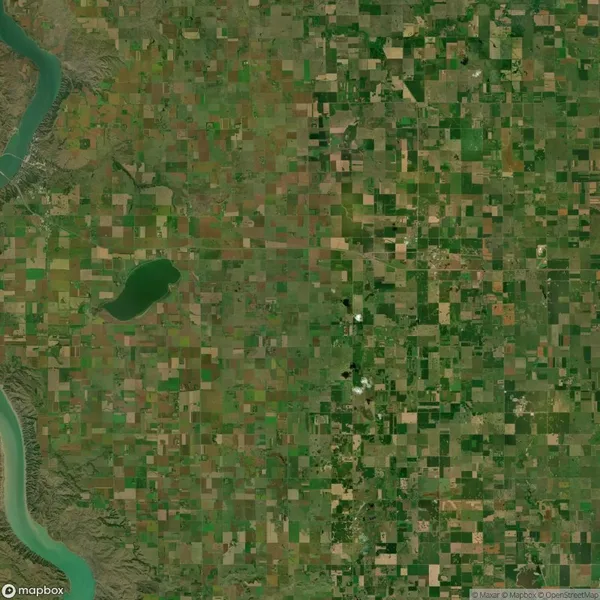 Aerial view of a vast patchwork landscape of green and brown agricultural fields, a river on the left, and a small lake in the center.