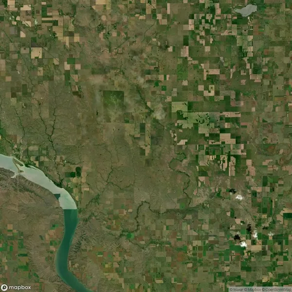 Aerial view of an agricultural landscape with patchwork fields, a meandering river on the bottom left, and a mix of brown and green areas, indicating varying stages of crop growth.
