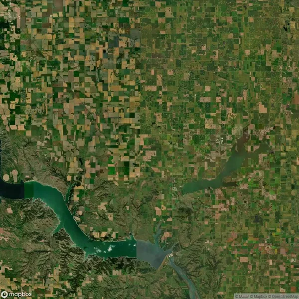 Aerial view of a green and brown patchwork farmland landscape, with a winding river and hills in the lower-left corner.