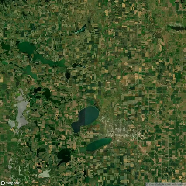 Aerial view of a patchwork agricultural landscape with numerous rectangular fields, several lakes, and a small urban area with roads in the center.