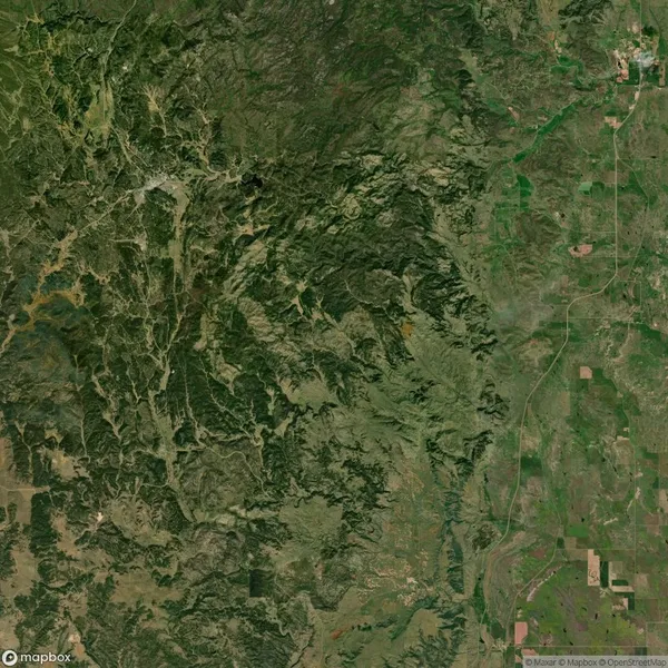 Satellite view of a mountainous region on the left with dense greenery, transitioning to flatter, sparsely vegetated terrain on the right.