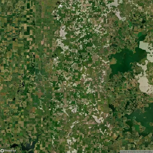 Aerial view of a patchwork landscape featuring green and brown fields, scattered wooded areas, and bodies of water, depicting a rural region.