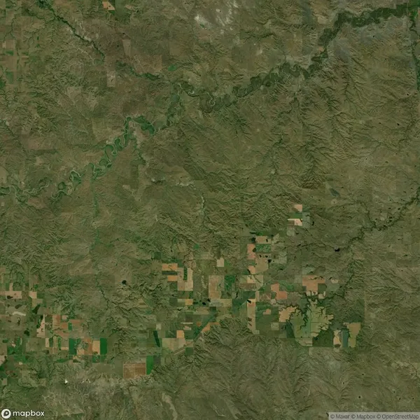 Satellite view of a landscape featuring agricultural fields in a grid pattern, surrounded by a mix of grassy and rocky terrain, with a river visible in the upper section.