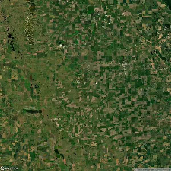 Aerial view of a vast, patchwork landscape comprising fields and farmland. The area is predominantly green with scattered patches of brown and gray, indicating varying land use and vegetation.