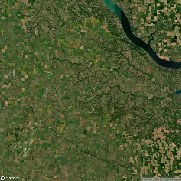 Aerial view of a patchwork landscape featuring agricultural fields, a winding river on the right, and varying terrain elevation, possibly indicating a mix of farmlands and natural formations.