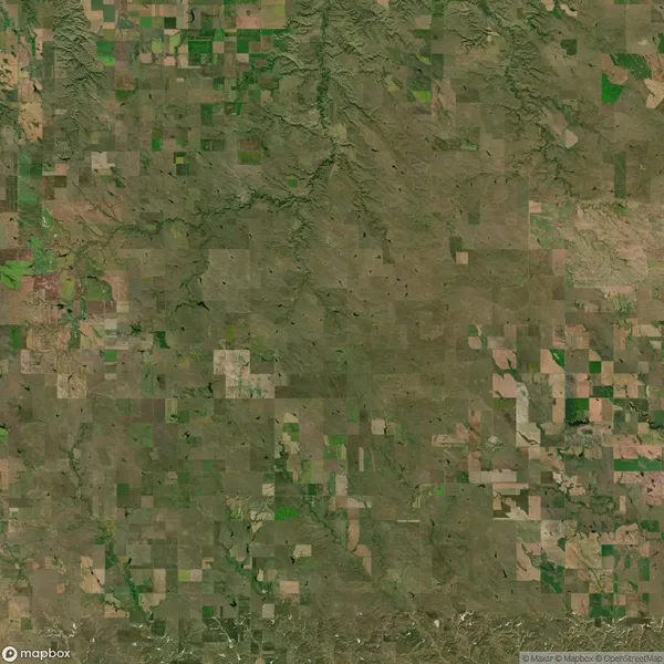 Aerial view of a patchwork landscape featuring numerous green and brown rectangular agricultural fields. The fields are intersected by various narrow roads and natural features.