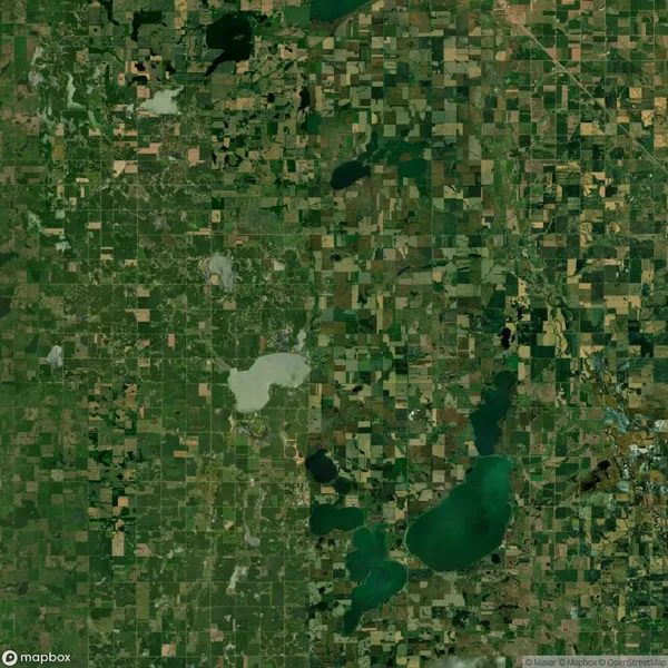 Aerial view of a grid-like patchwork of green and brown agricultural fields interspersed with several lakes and ponds.