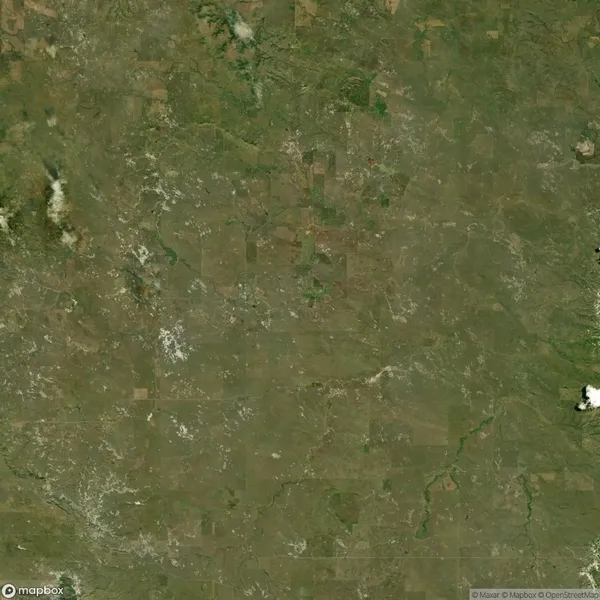 Aerial view of a vast expanse of green and brown land with scattered white patches, indicating sparse vegetation and clouds. No visible human structures or bodies of water.