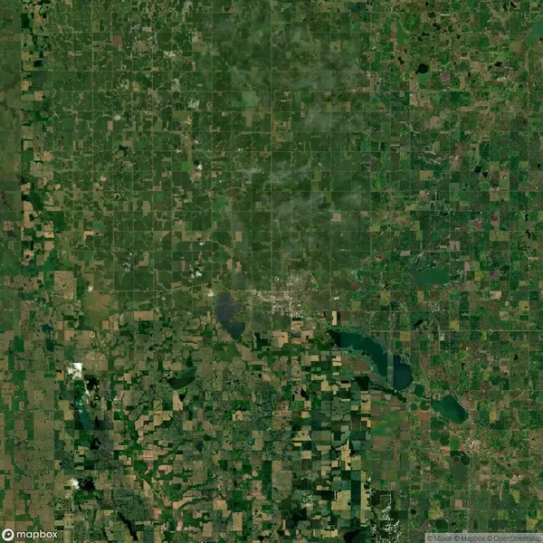 Satellite view of a landscape showing a grid of green farmland, fields, and patches of woodland with a few bodies of water.