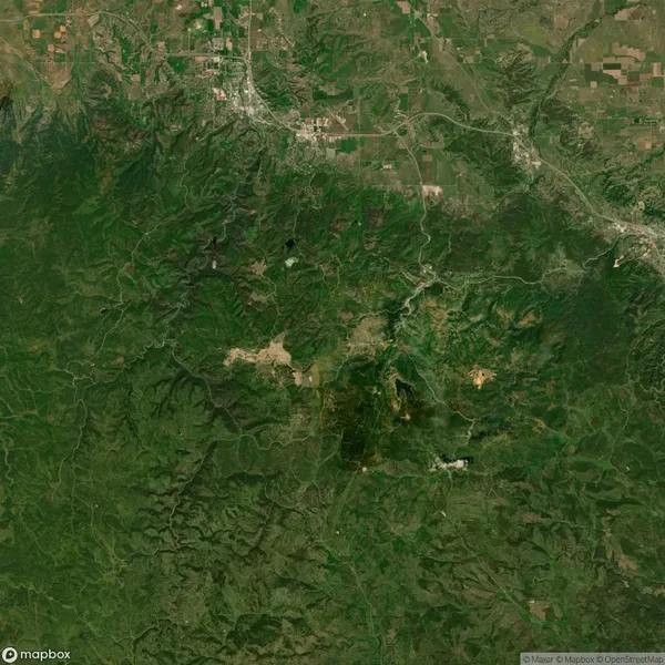 Satellite view of a lush green landscape with visible roads, patches of farmland, and scattered settlements, surrounded by dense forest areas.
