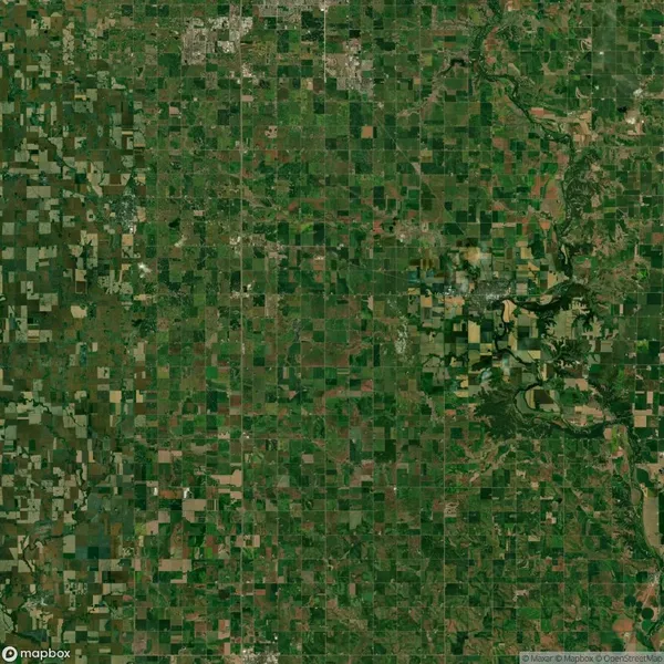 Aerial view of a vast, green patchwork of agricultural fields and a river curving through the landscape. Sparse rural settlements dotted across the area.