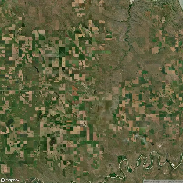 Aerial view of a rural landscape with patchwork farmland and a meandering river in the lower right corner. Various shades of green and brown indicate different types of fields.