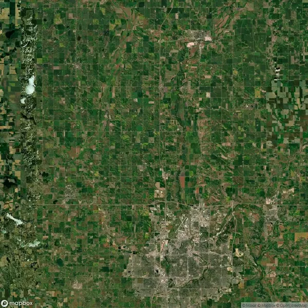 Aerial view of a rural landscape with a grid of roads, fields, and patches of forests. A denser urban area is visible at the bottom of the image.