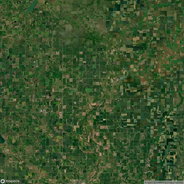 Aerial view of a large, patchwork agricultural landscape with fields and farmlands in varying shades of green and brown, interspersed with roads and small water bodies.