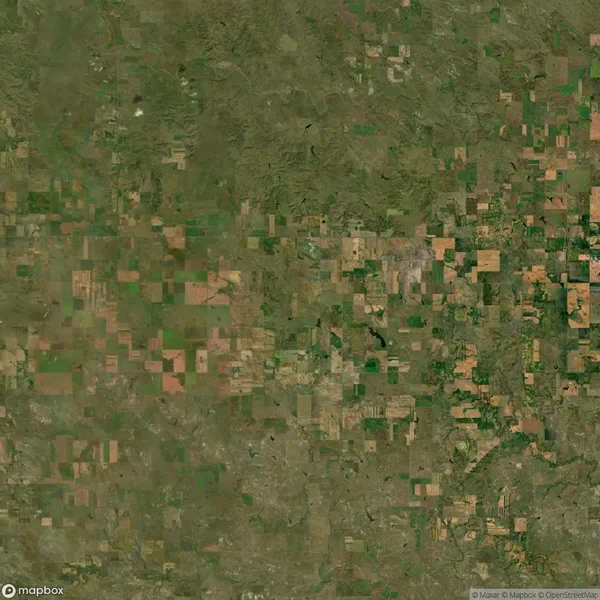 Aerial view of agricultural land with patchwork fields in various shades of green and brown, likely depicting farmland or rural landscape.