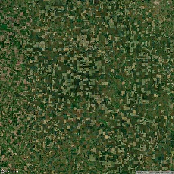 Aerial view of a rural landscape with numerous square and rectangular agricultural plots in varied shades of green and brown, forming a patchwork pattern.