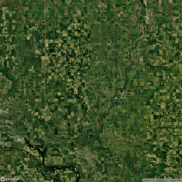 Aerial view of a landscape divided into agricultural fields with varied green tones, intersected by a winding river. Patches of forest are visible throughout.