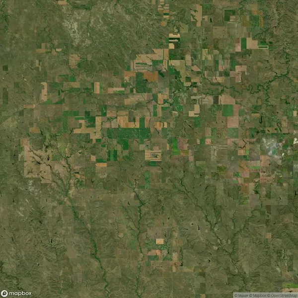 Aerial view of a patchwork of agricultural fields with varied shades of green and brown, intersected by roads and natural waterways.