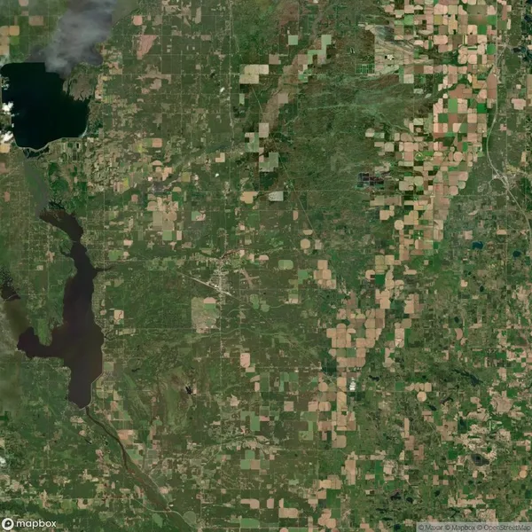 Aerial view of a green and brown patchwork of agricultural fields, with a few lakes visible on the left side of the image.