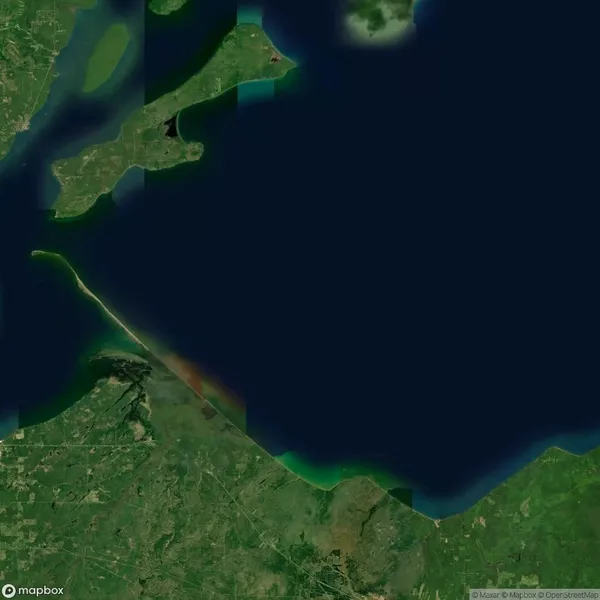 Satellite image of a coastal region with a thin land strip extending into the water, surrounded by green land areas and a large body of water.