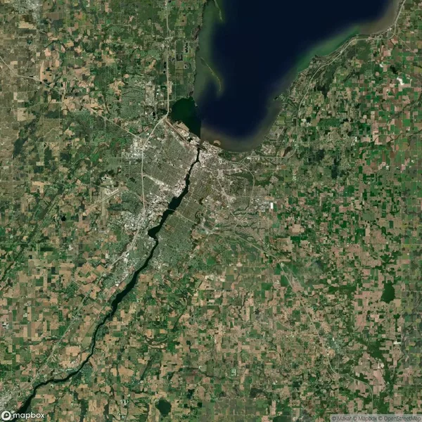 Satellite view of a city with a river flowing through it, surrounded by rural and agricultural land, with a large lake at the top.