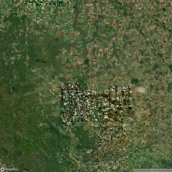 Satellite view of fragmented green and brown agricultural fields surrounding a dense, irregular urban area with visible streets and buildings.