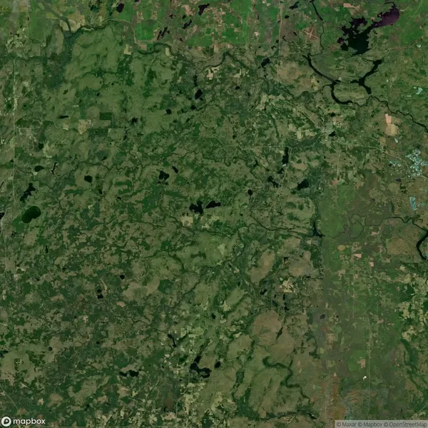 Aerial view of a landscape with various shades of green, indicating fields, forests, and bodies of water scattered throughout. Sparse roads and scattered settlements are visible.