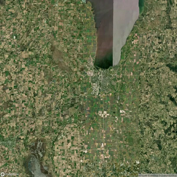 Aerial view of farmland surrounding a town near a large body of water, with a patchwork pattern of fields.