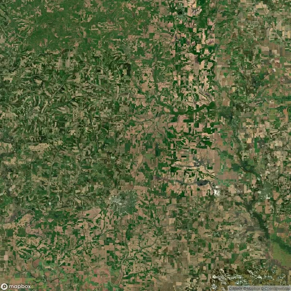 Satellite view of a mixed landscape with patches of green vegetation and brown fields, intersected by roads and waterways.