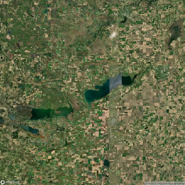 Aerial view of a landscape with a mosaic of agricultural fields, several lakes, and winding rivers. The area showcases a mix of green and brown patches.