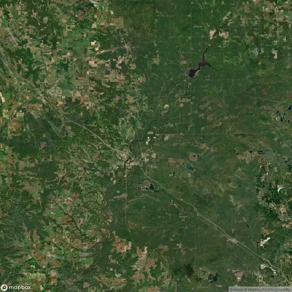 Satellite image showing a mix of urban and rural areas with patches of agricultural land, roads, and water bodies, likely in a region with diverse terrain and development patterns.