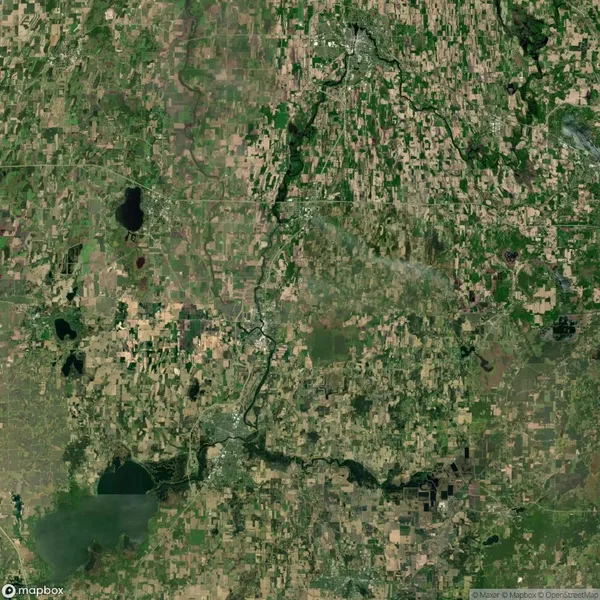 Satellite view of a large, mostly green and brown landscape with scattered patches of vegetation, fields, and a winding river running vertically through the center. Visible lakes and roads.