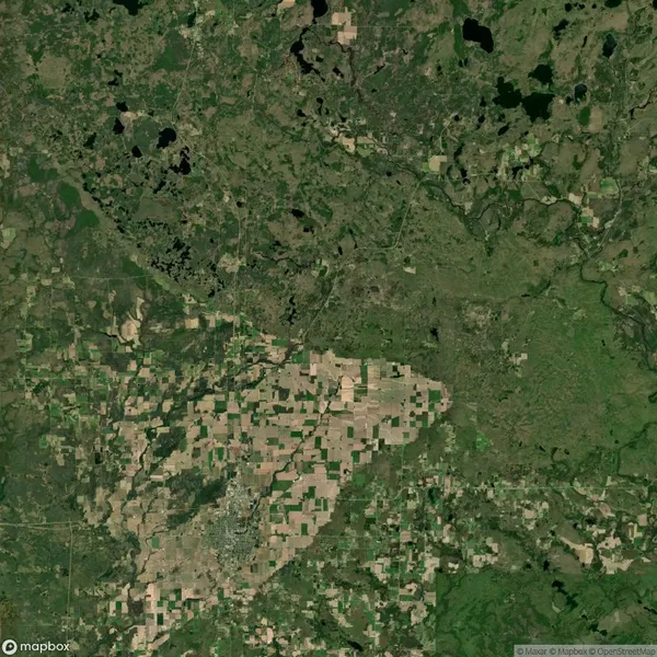 Aerial view of a landscape showing a patchwork of agricultural fields, surrounded by forests and water bodies, with varying shades of green and brown.