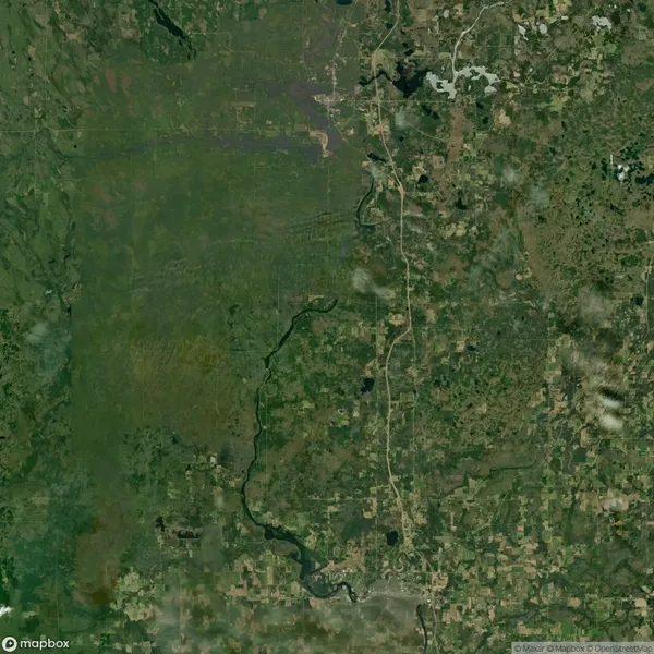 Satellite image of a green and brown landscape with a winding river and scattered clouds. Roadways and patches of vegetation are visible throughout the area.