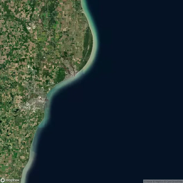 Satellite view of a coastline with farmland and urban areas on the left and a body of water on the right.