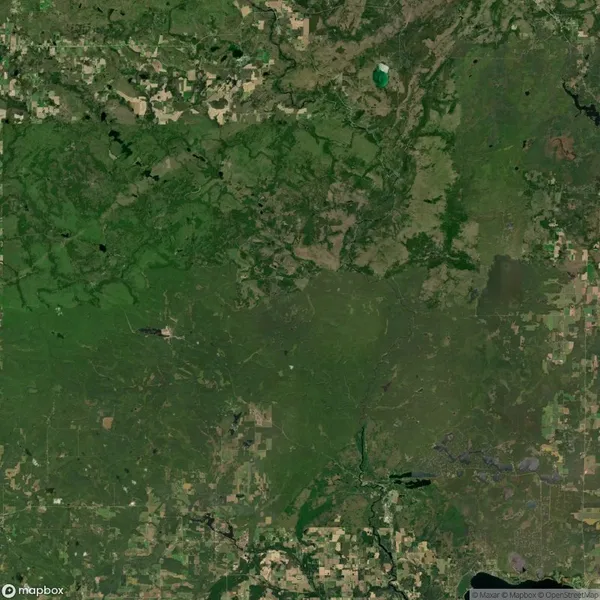 Aerial view of a landscape with green fields, patches of woodland, and scattered clearings. Roads and small bodies of water are visible throughout the area.