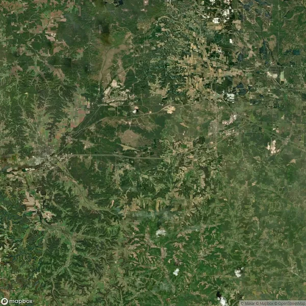 Aerial view of a green landscape with scattered patches of urban development and road networks, surrounded by various shades of green vegetation and farmland.