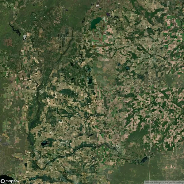 Aerial view of a rural landscape featuring patches of green vegetation, agricultural fields, and scattered water bodies, intersected by roads and a river winding through the scene.