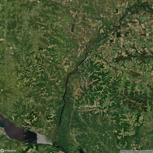 Satellite view of a landscape showing a winding river flowing through a mix of forests, fields, and agricultural areas. There are visible land patterns and a body of water at the bottom.