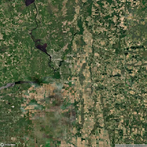 Aerial view of a landscape featuring a mix of green and brown agricultural fields, forests, and a meandering river intersecting a small urban area.