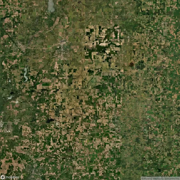 Aerial view of a large patchwork of agricultural fields and forested areas, showing various shades of green and brown.