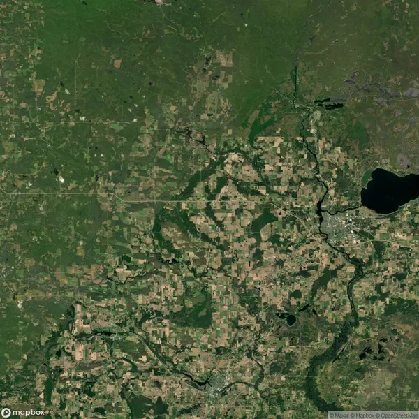 Satellite view of a landscape featuring a mix of green farmland and patches of forest, intersected by a winding river, with a large dark lake on the right side.
