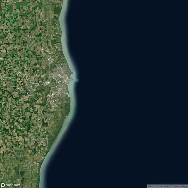 Satellite view of a coastal region showing farmland and urban areas on the left, with a large body of water on the right.