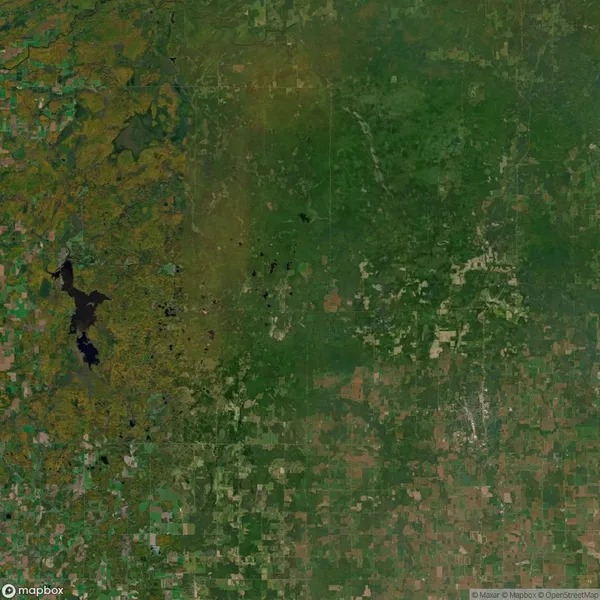 Satellite view of rural landscape with patchwork fields, a large dark lake on the left, and varying shades of green and brown representing vegetation and terrain.