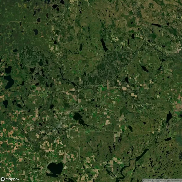 Satellite view of a rural landscape with patches of cultivated land, forests, and several lakes. A network of roads and a main highway run through the central area.